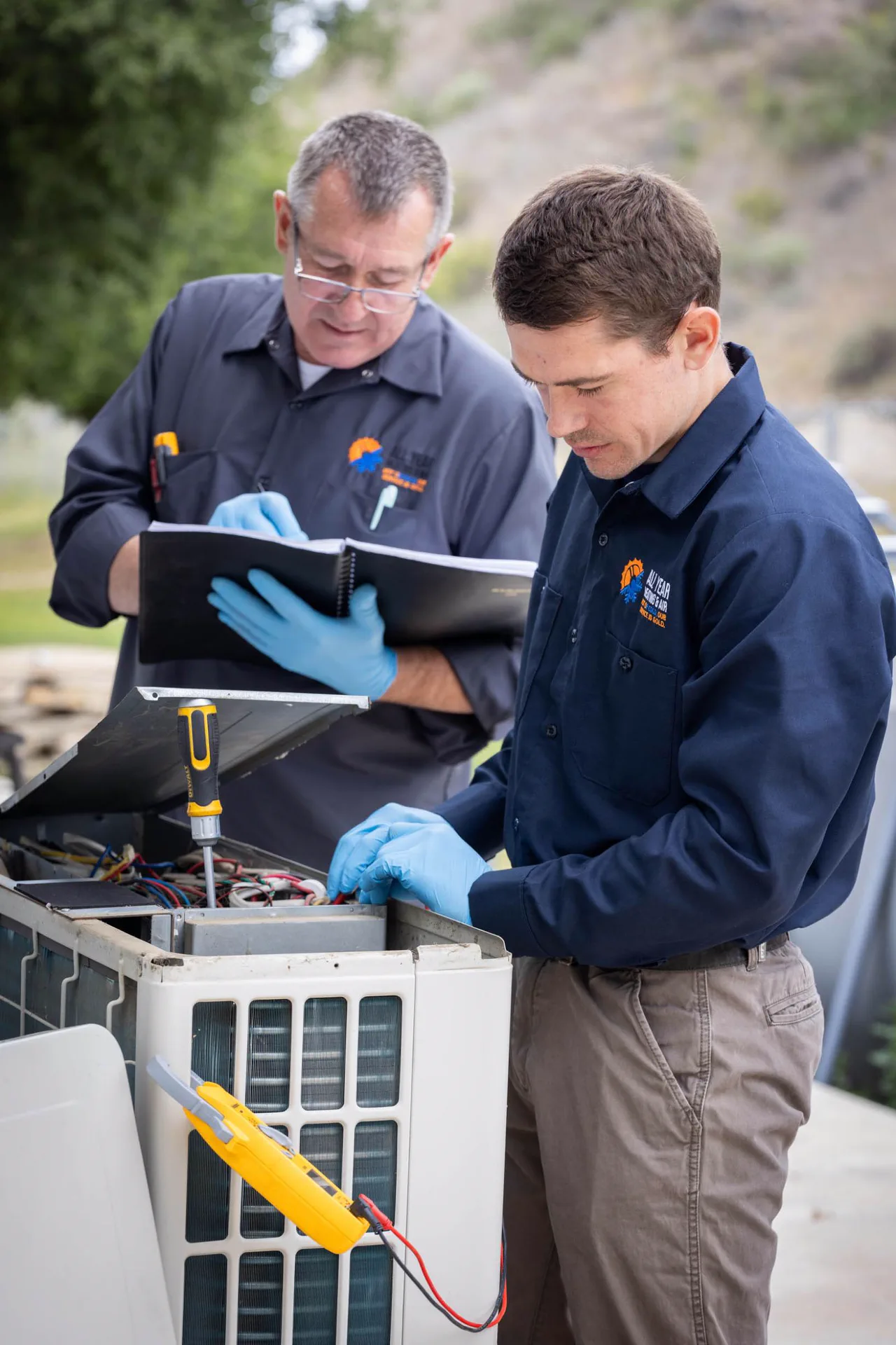 All Year Heating & Air technician inspecting an outdoor AC unit and writing notes